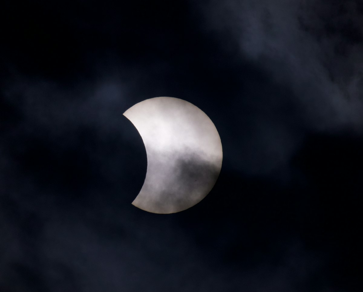 A partial solar eclipse obscured by dark clouds in the night sky