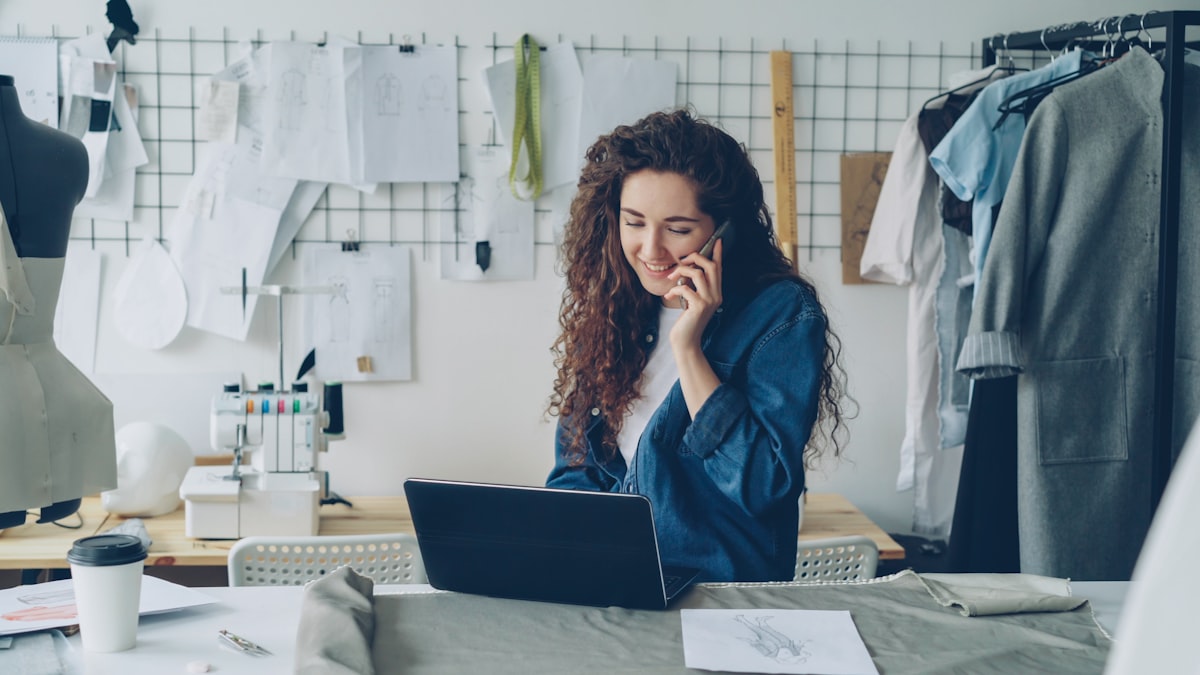 Fashion designer on the phone, working on a laptop.