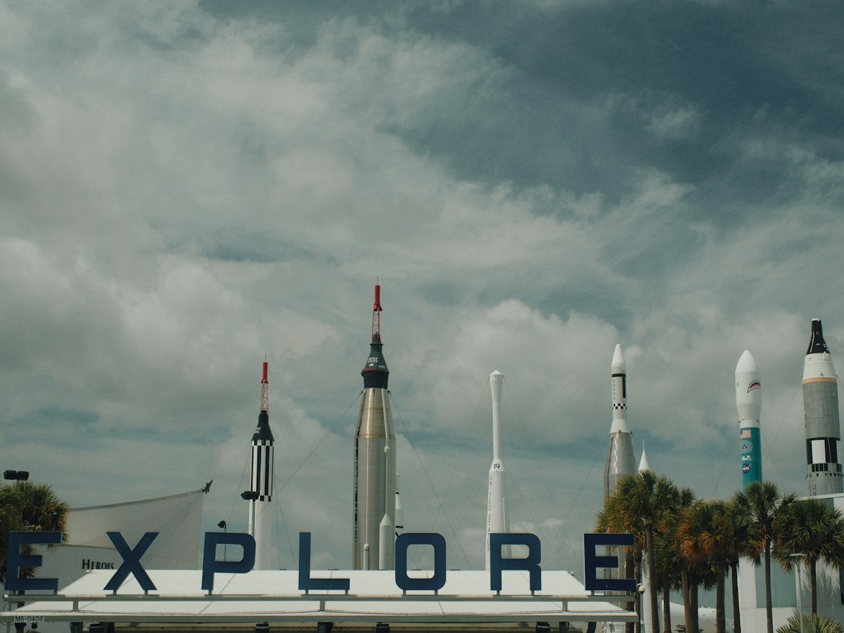 Rockets stand tall behind an 'explore' sign under cloudy sky