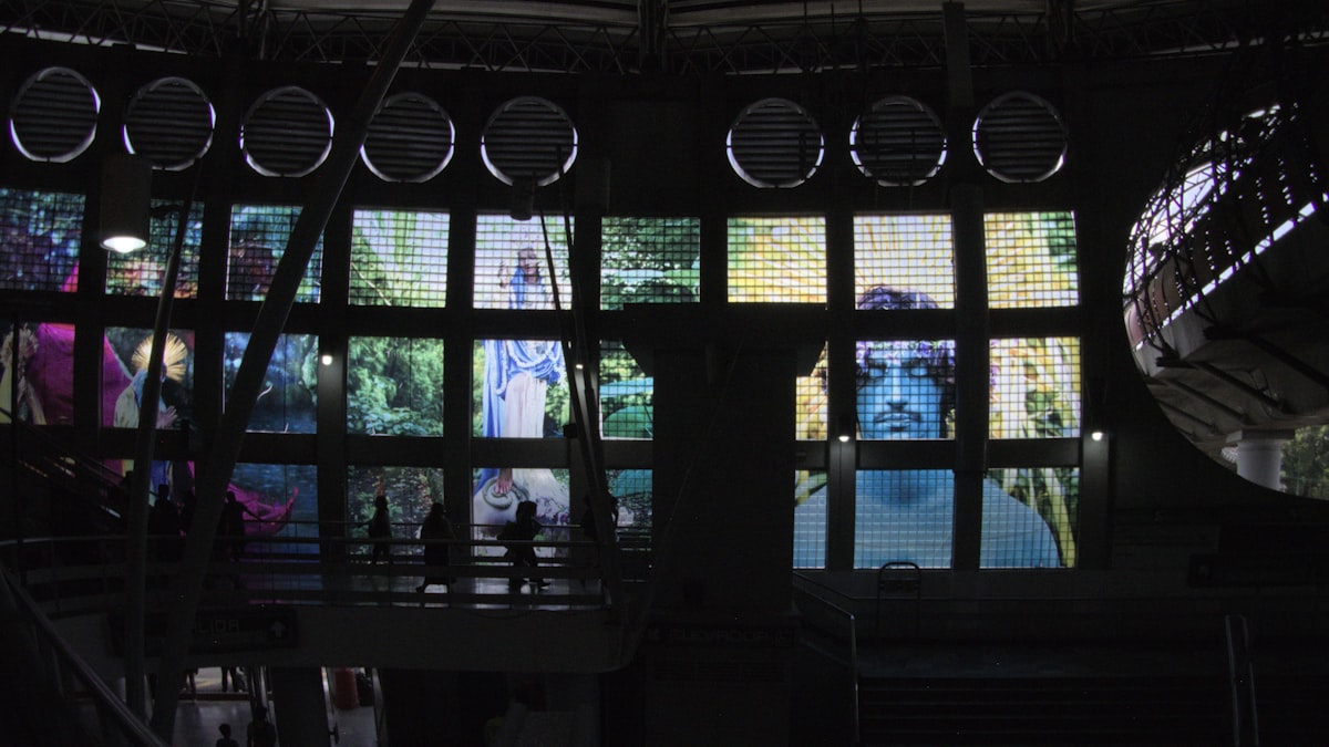 Silhouetted people walking past a large grid of illuminated stained glass windows