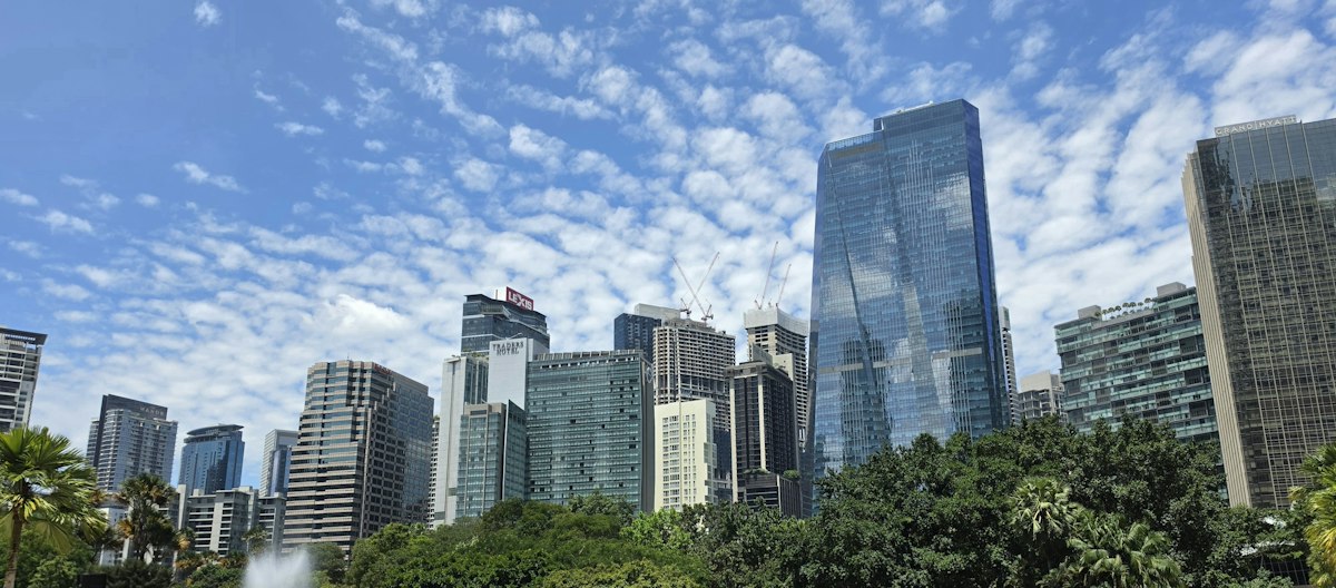 City skyline with modern skyscrapers, green trees, and cloudy sky