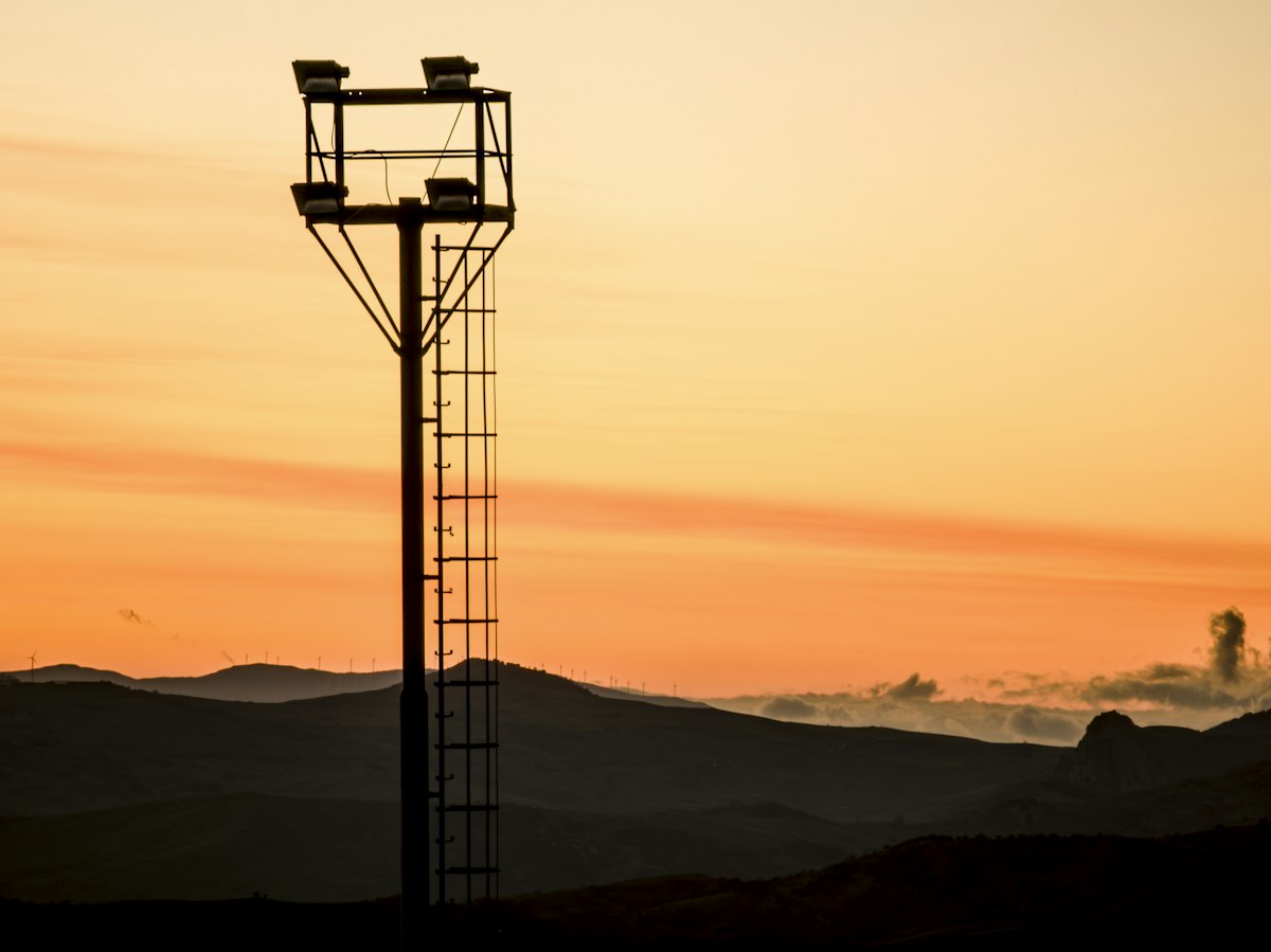 Tall industrial tower silhouetted against an orange sunset sky