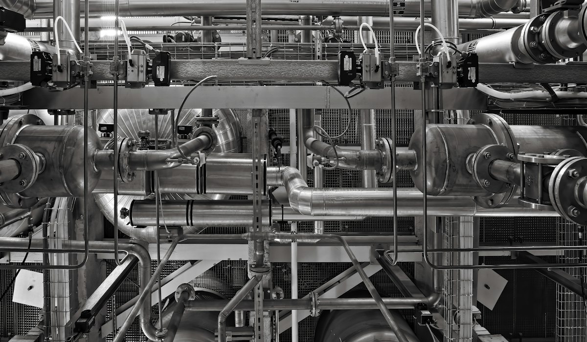 A complex network of industrial metal pipes and valves in a factory setting
