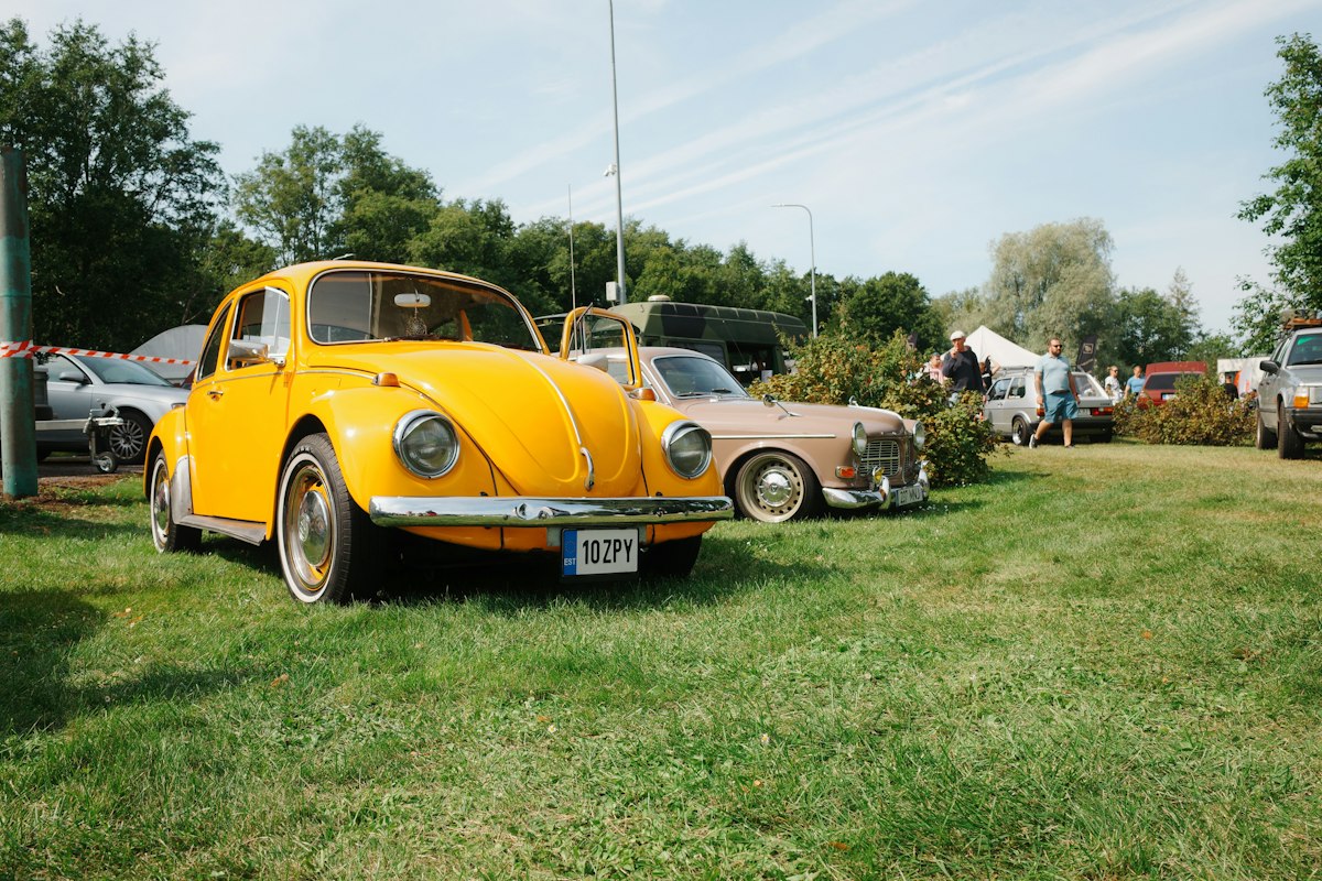 A bright yellow vintage Volkswagen Beetle parked on a grassy field at a car show