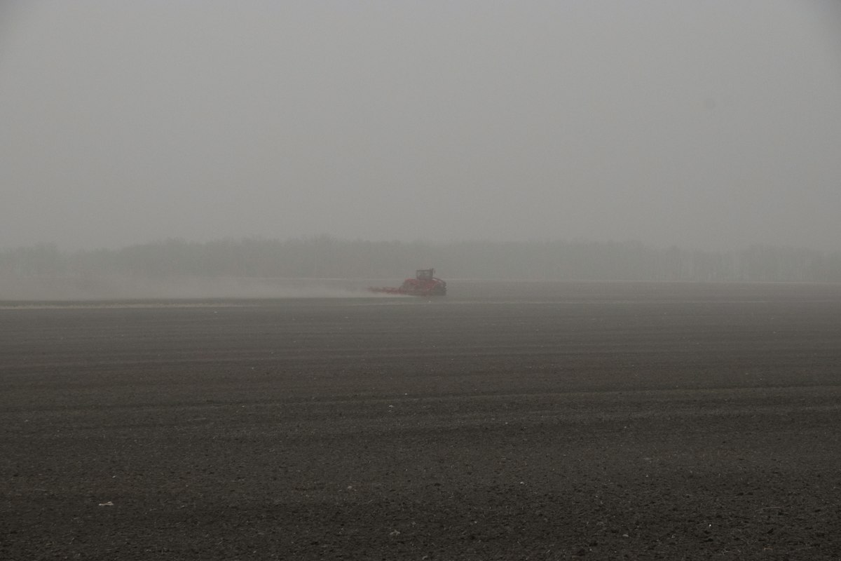 A tractor working in a dusty, hazy field