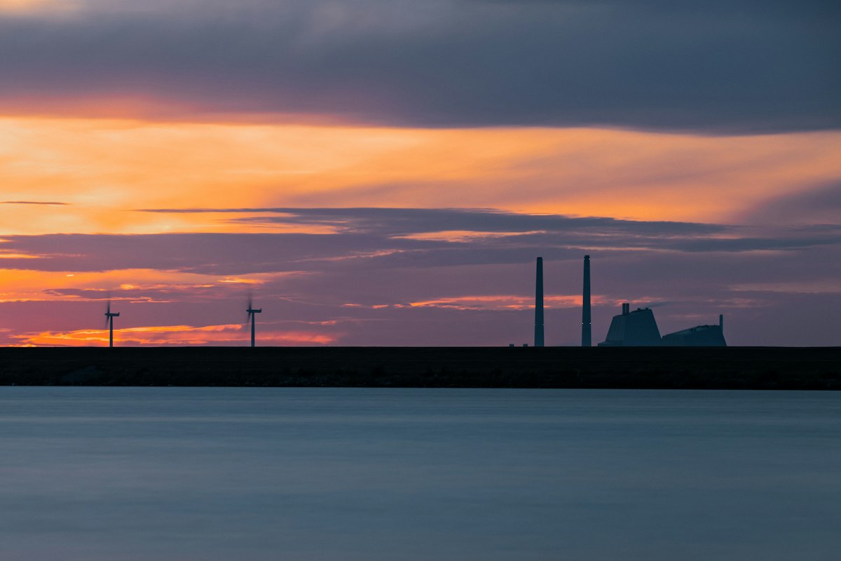 Wind turbines and a power plant silhouette against a warm orange sky