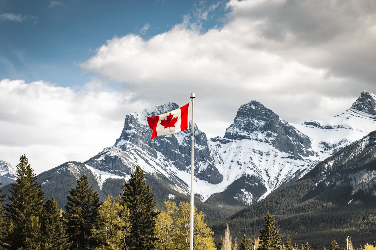 The Canadian flag waving on a pole before the Three Sisters mountains in Canmore
