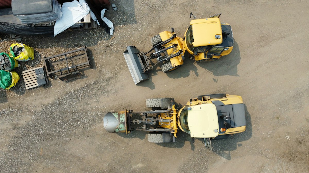 Two yellow construction vehicles parked on gravel