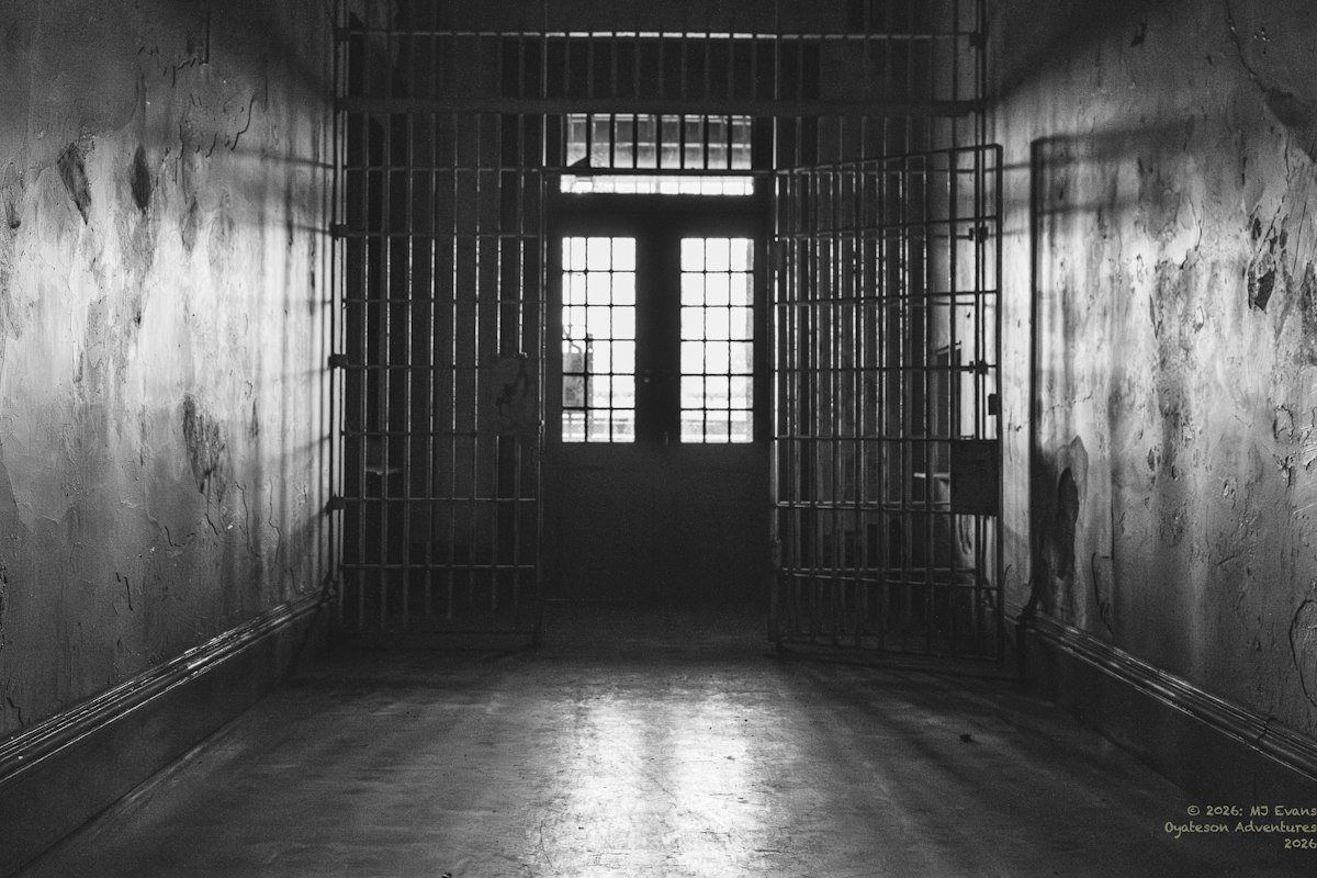 A dark, empty prison hallway with cell doors open