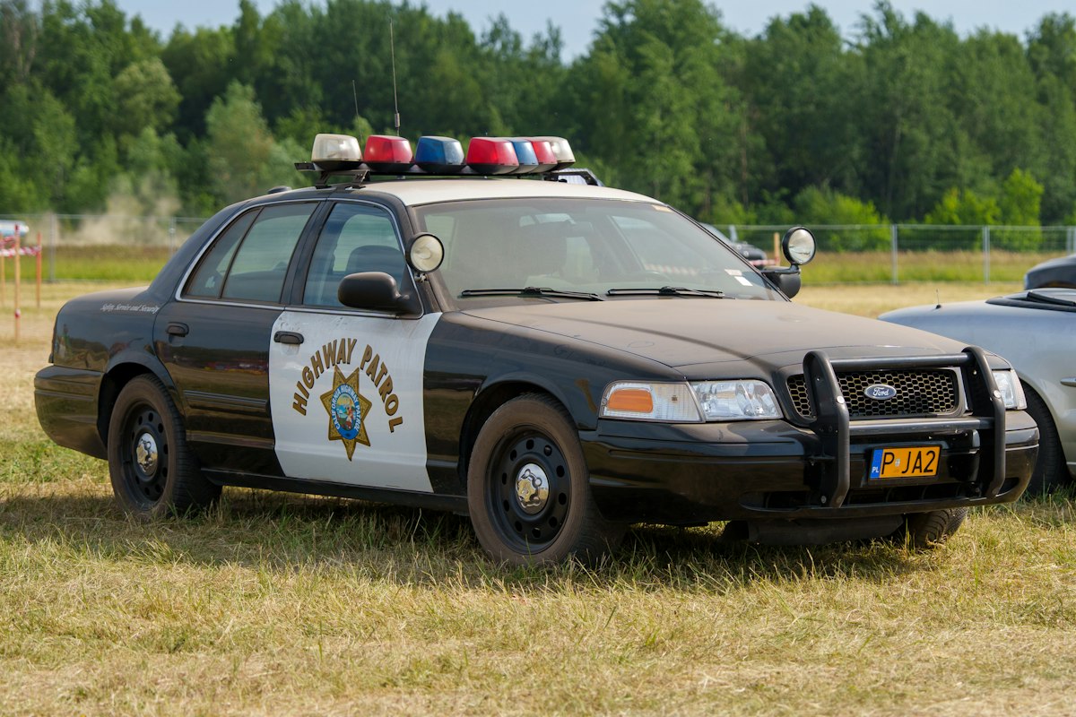 A black and white highway patrol car parked on grass