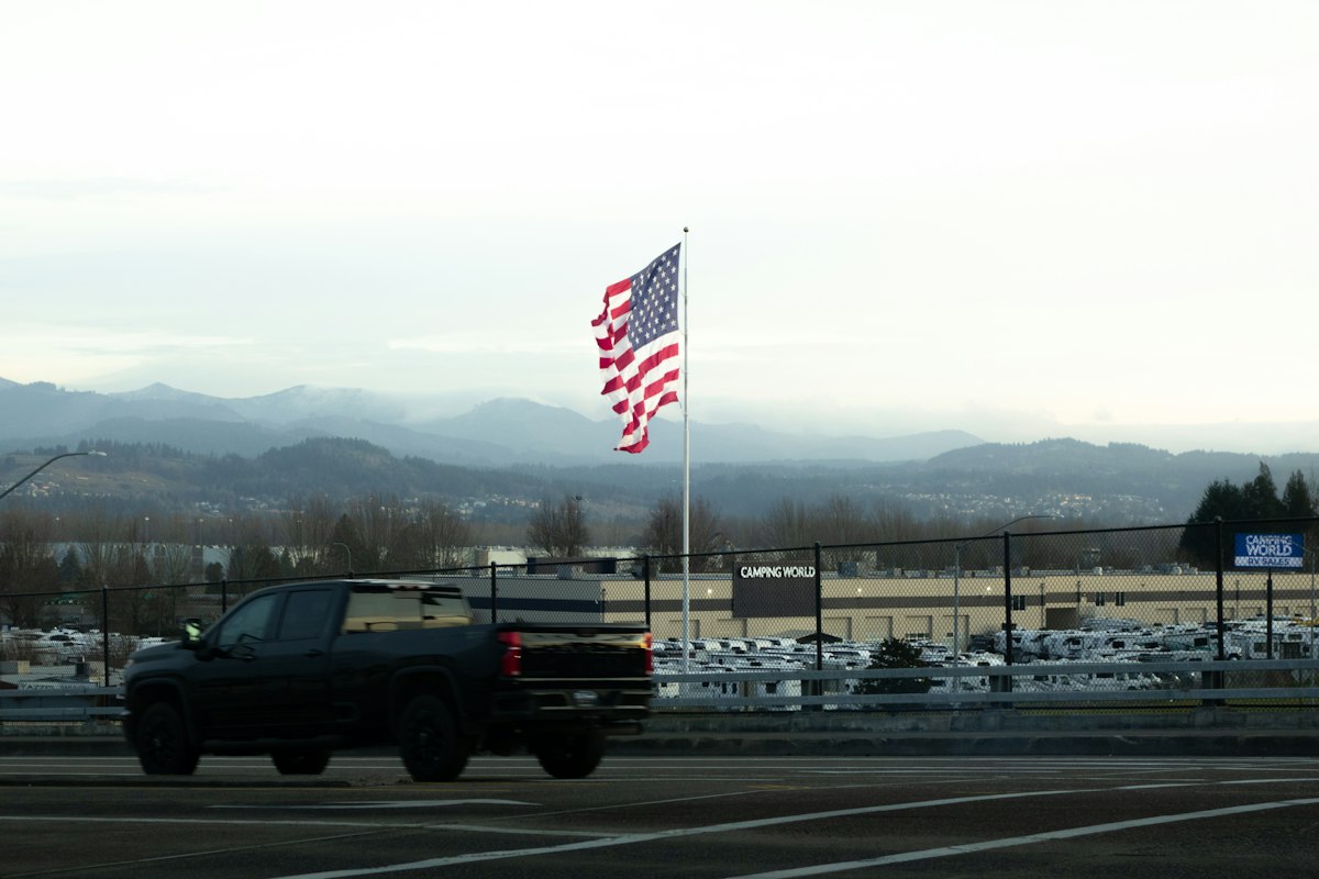 American flag waves near a dark truck and mountains