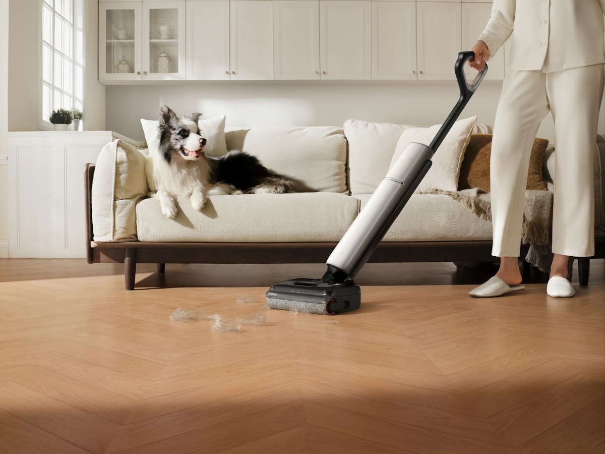 A person vacuums a wooden floor while a dog watches