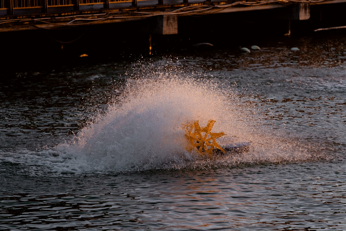a yellow boat splashing in the water near a bridge
