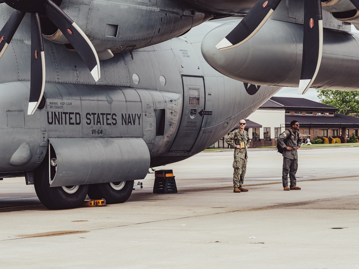 Two navy personnel stand by a military aircraft.